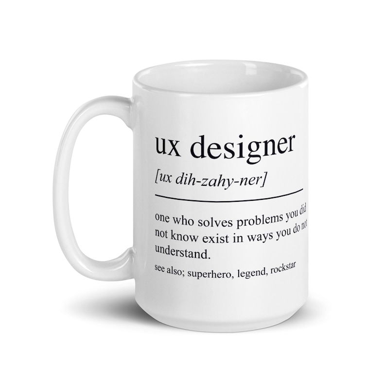 Op de afbeelding: Een witte keramische mok met de zwarte tekst "ux designer" en een definitie. De definitie bevat de uitspraak en een beschrijving van een UX-ontwerper. De mok heeft een gebogen handvat.