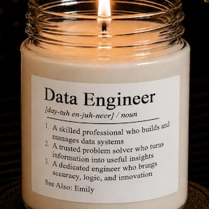 May include: A clear glass jar candle with a lit wick and white wax. The label features the text: Data Engineer [day-tuh en-juh-neer] / noun 1. A skilled professional who builds and manages data systems 2. A trusted problem solver 3. A dedicated engineer. See Also: Emily.