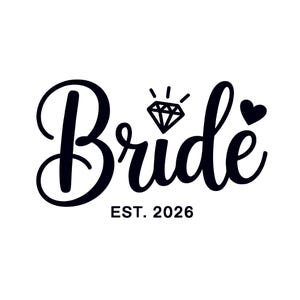 Puede incluir: Texto negro en cursiva sobre fondo blanco: "Bride", con un diamante y un corazón. Debajo, "EST. 2026". Ideal para artículos de temática nupcial, como camisetas o accesorios.