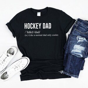 May include: Black t-shirt with white text that reads "HOCKEY DAD /'h&auml;kē//dad/ (n.) Like a normal dad only cooler."