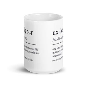 Op de afbeelding: Witte keramische mok met de tekst "ux designer" en een definitie aan de zijkant. De definitie bevat zinnen als "problemen die je hebt gedaan". De mok is cilindrisch en heeft een glanzende afwerking.