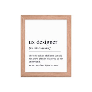 May include: A framed print with a white background and black text that reads "ux designer [ux dih-zahy-ner] one who solves problems you did not know exist in ways you do not understand. see also; superhero, legend, rockstar"