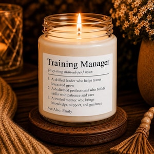 Op de afbeelding: Een kaars in een doorzichtige glazen pot met een wit etiket met de tekst Training Manager, een fonetische uitspraak en drie definities die een bekwame leider, een toegewijde professional en een vertrouwde mentor beschrijven.