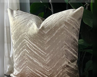 May include: A square throw pillow featuring a light beige and champagne chevron pattern with a textured, velvet-like finish. The text @THECHARMINGPILLOW is visible at the top. The pillow has a visible zipper closure along the top edge.