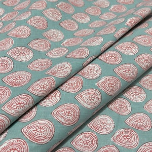 May include: Teal fabric with a repeating pattern of red and white teardrop shapes. The teardrop shapes have a decorative design inside.