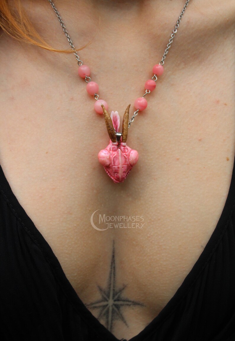 Pode incluir: Um colar com pingente de inseto rosa com corrente prateada e detalhes de contas rosa. O pingente tem antenas marrons e um design texturizado detalhado. O colar &eacute; uma pe&ccedil;a de joalheria &uacute;nica.