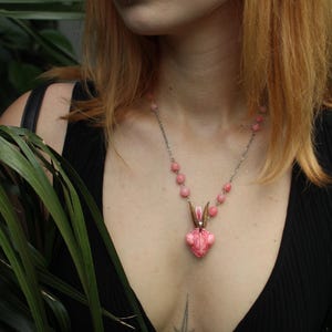 Pode incluir: Um colar com pingente de coelho rosa e corrente prateada. O pingente tem um design em forma de cora&ccedil;&atilde;o com rosto e orelhas de coelho. O colar &eacute; usado por uma pessoa com um top preto. O logotipo Moonphases Jewellery &eacute; vis&iacute;vel.