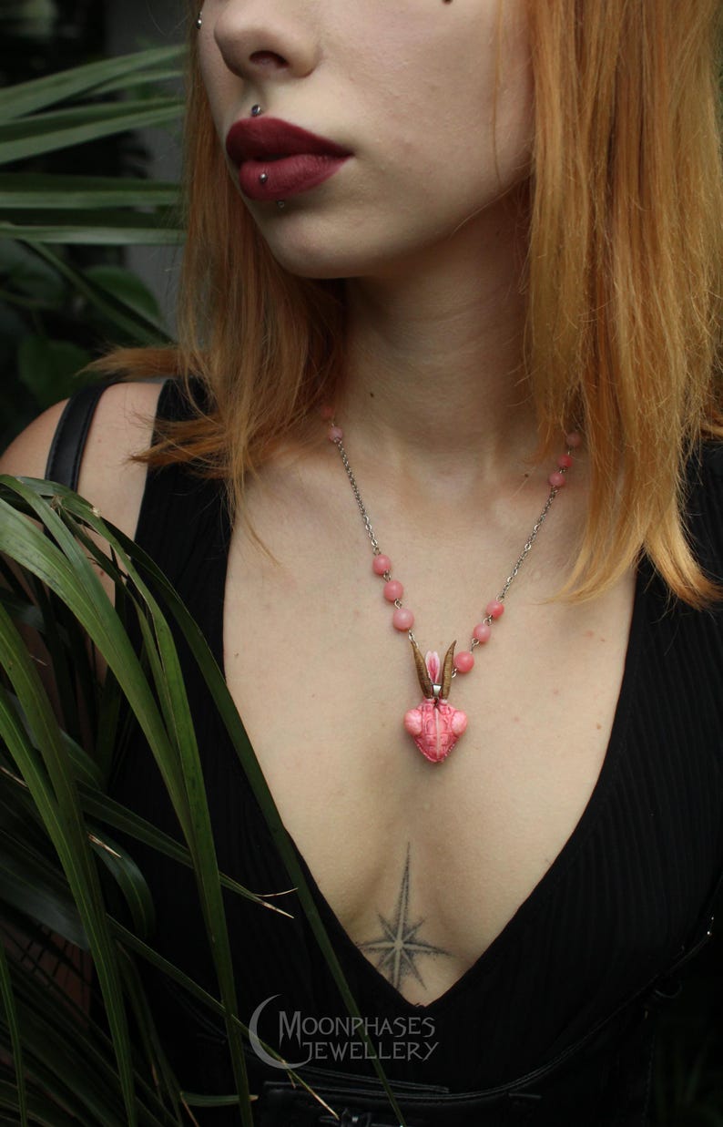 Pode incluir: Um colar com pingente de coelho rosa e corrente prateada. O pingente tem um design em forma de cora&ccedil;&atilde;o com rosto e orelhas de coelho. O colar &eacute; usado por uma pessoa com um top preto. O logotipo Moonphases Jewellery &eacute; vis&iacute;vel.