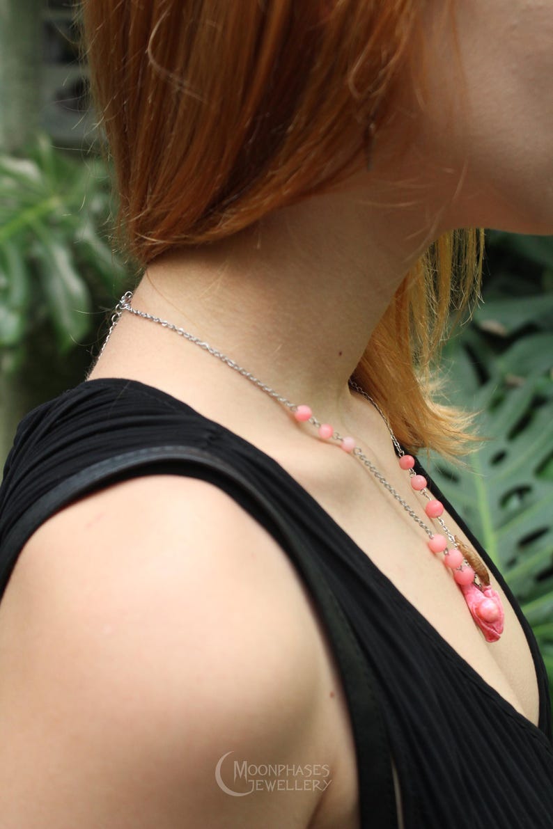 Pode incluir: Um colar de corrente prateada com contas rosa e um pingente rosa. O colar &eacute; usado sobre um top preto. O logotipo Moonphases Jewellery &eacute; vis&iacute;vel na parte inferior.