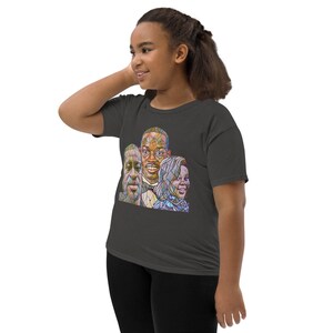 May include: A dark gray youth t-shirt with a colorful stained glass style portrait of three people. The portrait features a man with glasses and a bow tie, a woman with a blue scarf, and a man with a beard.