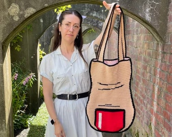 May include: A crocheted tote bag shaped like a finger with a red nail polish design. The bag is held by a person wearing a white dress and glasses.