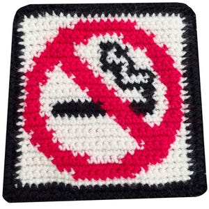 May include: A square, crocheted patch with a black border. The center features a red circle with a diagonal line through a black cigarette, indicating a no-smoking symbol. The background is white.