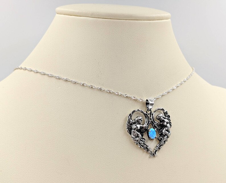 May include: A silver necklace with a heart-shaped pendant featuring two angels holding a blue opal gemstone.