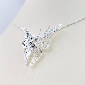 May include: A silver butterfly pendant necklace with a delicate, intricate design. The butterfly is suspended from a thin silver chain.