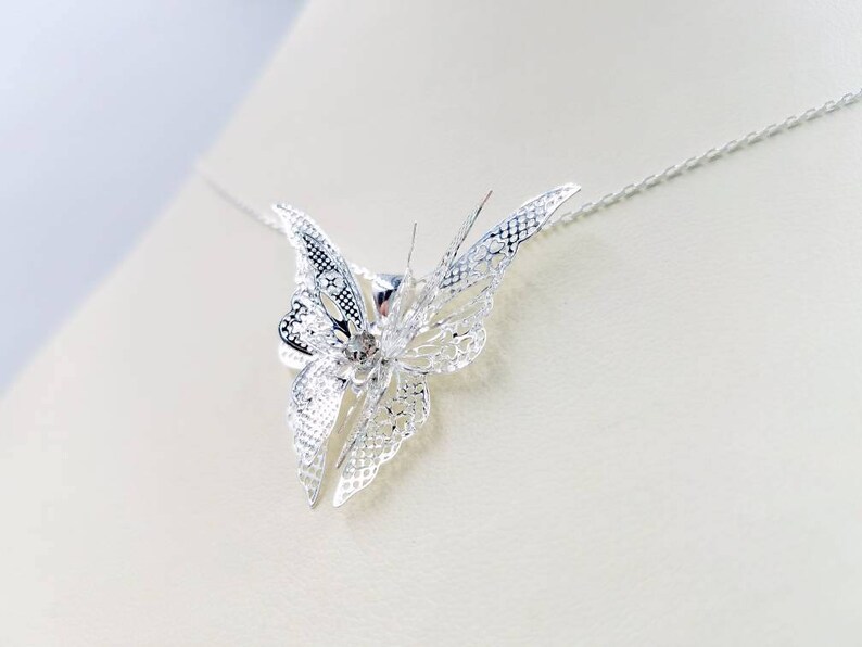 May include: A silver butterfly pendant necklace with a delicate, intricate design. The butterfly is suspended from a thin silver chain.