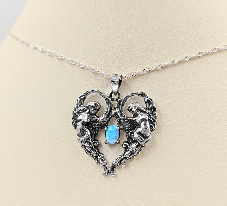 May include: A silver necklace with a heart-shaped pendant featuring two angels with wings and a blue opal gemstone in the center.