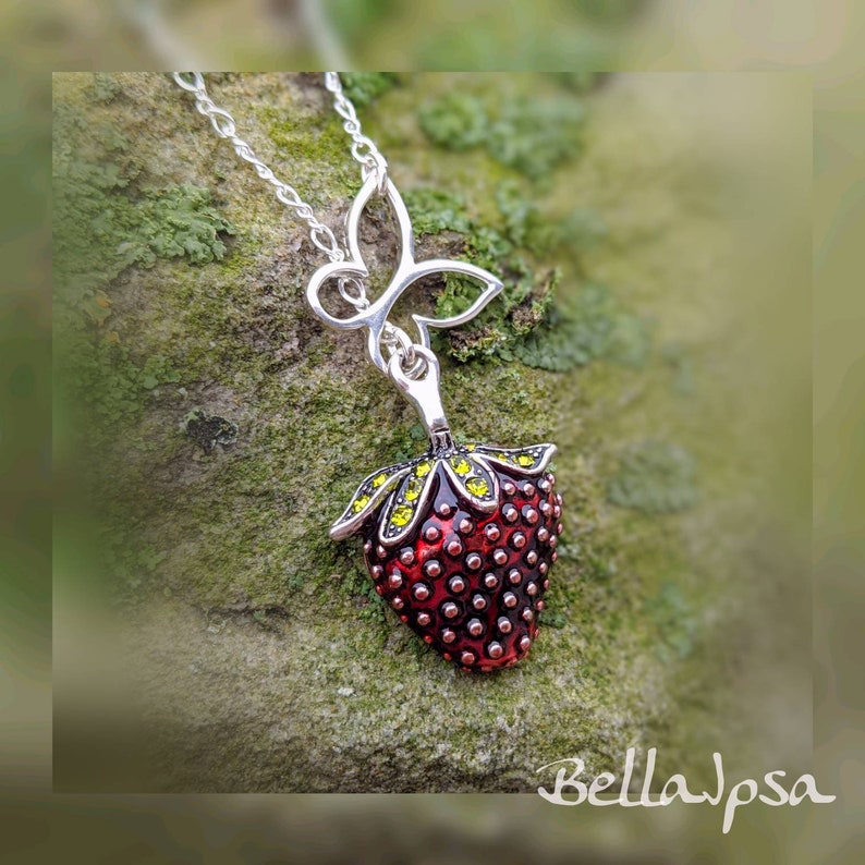 Peut inclure: Un collier en argent avec un pendentif en forme de fraise rouge et verte et un pendentif en forme de papillon. Le pendentif est recouvert de petits cristaux rouges et verts.
