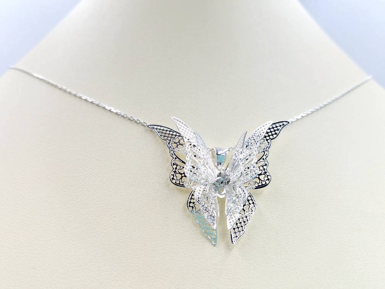 May include: A silver necklace with a delicate butterfly pendant. The butterfly is made of intricate filigree work and has a slightly iridescent finish.