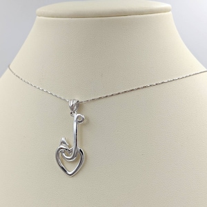 May include: A silver pendant necklace with a heart and hook design. The pendant hangs from a fine chain, shown on a mannequin. The heart is open, and the hook curves around it. The necklace is made of a shiny metal, and is displayed on a mannequin.