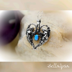 May include: A silver pendant necklace featuring two angels forming a heart shape with a blue opal gemstone in the center.
