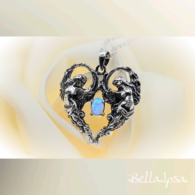 May include: A silver heart-shaped pendant with two angels on either side of a blue opal gemstone. The pendant is on a silver chain.