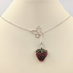 Peut inclure: Un collier en cha&icirc;ne argent avec un pendentif en forme de fraise et un pendentif en forme de papillon. La fraise est rouge avec des feuilles vertes et le papillon est argent&eacute;.