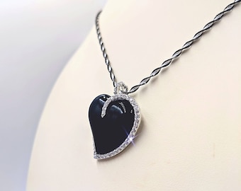 Puede incluir: Un collar de plata con un colgante de corazón negro adornado con brillantes transparentes.