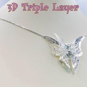 May include: A silver necklace with a 3D triple layer butterfly pendant. The butterfly is made of delicate filigree work and has a light blue center.