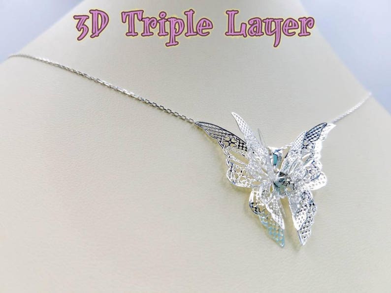 May include: A silver necklace with a 3D triple layer butterfly pendant. The butterfly is made of delicate filigree work and has a light blue center.