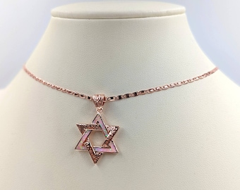 May include: A rose gold chain necklace with a pink opal Star of David pendant. The pendant has an intricate design with a filigree pattern.