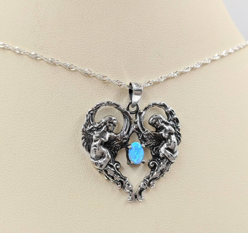 May include: A silver necklace with a heart-shaped pendant featuring two angels and a blue opal gemstone.