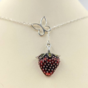 Peut inclure: Un collier en cha&icirc;ne argent avec un pendentif en forme de fraise et un pendentif en forme de papillon. La fraise est rouge avec des feuilles vertes et des graines noires. Le papillon est argent&eacute; et a les ailes d&eacute;ploy&eacute;es.
