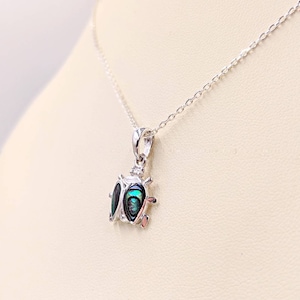 May include: A silver necklace with a green and blue abalone shell ladybug pendant.