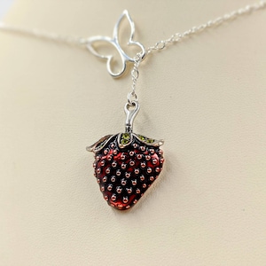 Peut inclure: Un collier en argent avec un pendentif en forme de fraise. La fraise est rouge avec des feuilles vertes et a une surface textur&eacute;e. Le collier comporte &eacute;galement un pendentif en forme de papillon argent&eacute;.