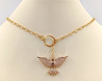 May include: A gold chain necklace with a delicate, open circle pendant. The pendant is attached to a small, sparkling, gold dove charm.