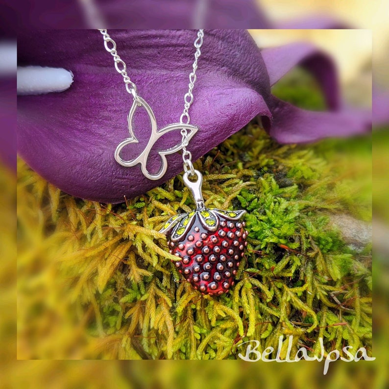 Peut inclure: Un collier en argent avec un pendentif en forme de papillon et une fraise rouge. La fraise est d&eacute;taill&eacute;e avec des feuilles vertes et de l'&eacute;mail rouge.