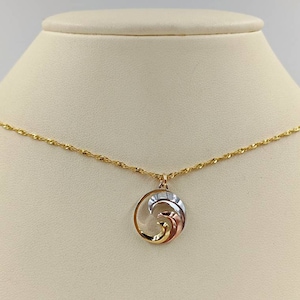 Pode incluir: Um colar de ouro com um pingente que apresenta um design de onda tridimensional em ouro e metal branco.