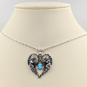 May include: A silver necklace with a heart-shaped pendant featuring two angels holding a blue opal gemstone.
