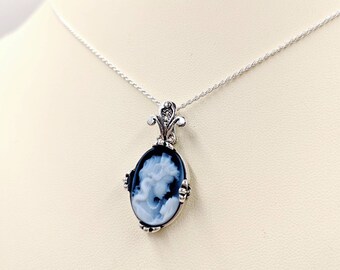 May include: A silver chain necklace with a cameo pendant featuring a black and white portrait of a woman. The pendant has a decorative silver filigree design.