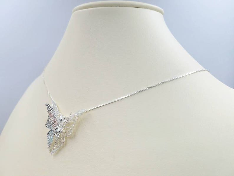 May include: A silver necklace with a delicate butterfly pendant. The butterfly is made of intricate filigree work and has a slightly iridescent finish.