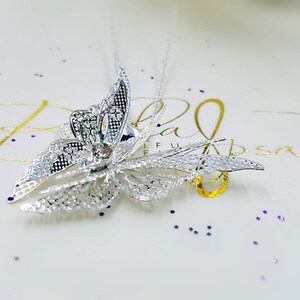 May include: A silver butterfly pendant necklace with a clear crystal in the center. The butterfly is detailed with intricate filigree work.