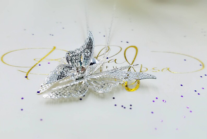 May include: A silver butterfly pendant necklace with a clear crystal in the center. The butterfly is detailed with intricate filigree work.