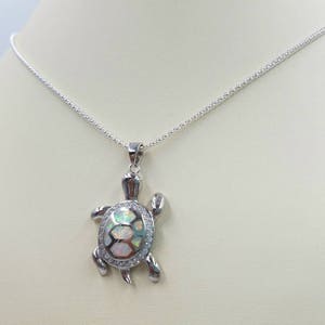 May include: A silver chain necklace with a silver turtle pendant. The turtle's shell is made of iridescent white opal.