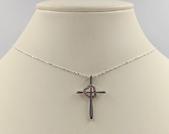 Puede incluir: Un collar de plata con una cadena delicada y un colgante con forma de cruz con un diseño de corazón. El corazón está adornado con piedras preciosas rosas.