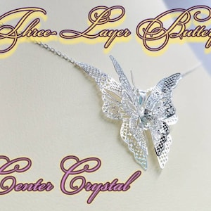 May include: Silver butterfly necklace with three layers of intricate detail and a clear crystal in the center. The necklace is on a white background.