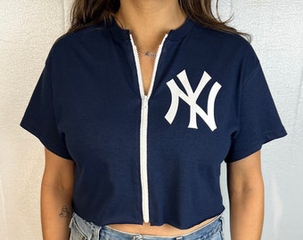May include: A navy blue cropped t-shirt with a white zipper down the front and a white New York Yankees logo on the front.