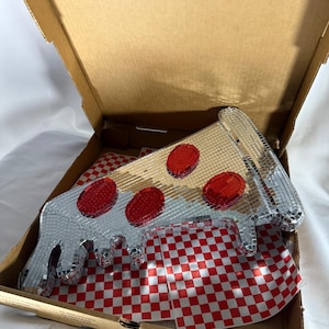 May include: A mirrored pizza slice with red pepperoni sits inside a cardboard pizza box. The pizza rests on a red and white checkered paper. The box is open, revealing the pizza and paper.