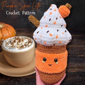 Könnte beinhalten: Häkelmuster für einen Pumpkin Spice Latte. Der Latte ist aus braunem und orangefarbenem Garn gefertigt und hat einen weißen Schlagsahne-Belag mit Schokoladenstreuseln. Der Latte hat ein süßes Gesicht mit braunen Augen und einem Lächeln.