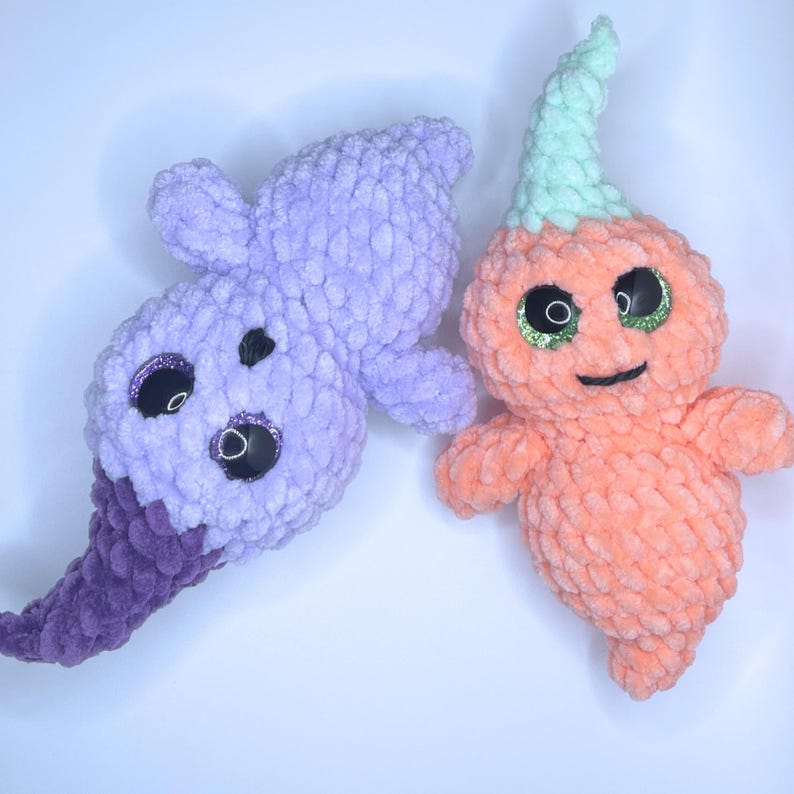 May include: Two crocheted ghost plushies, one is purple with a long tail and the other is orange with a green hat.