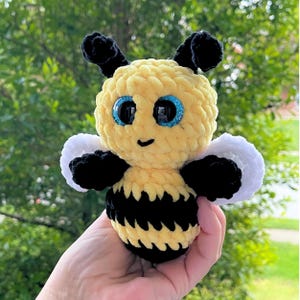 May include: A crocheted bee plush toy with black and yellow stripes, white wings, and large blue eyes.